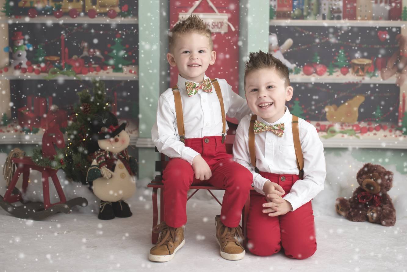 two young boys sitting on a bench in front of a christmas tree
