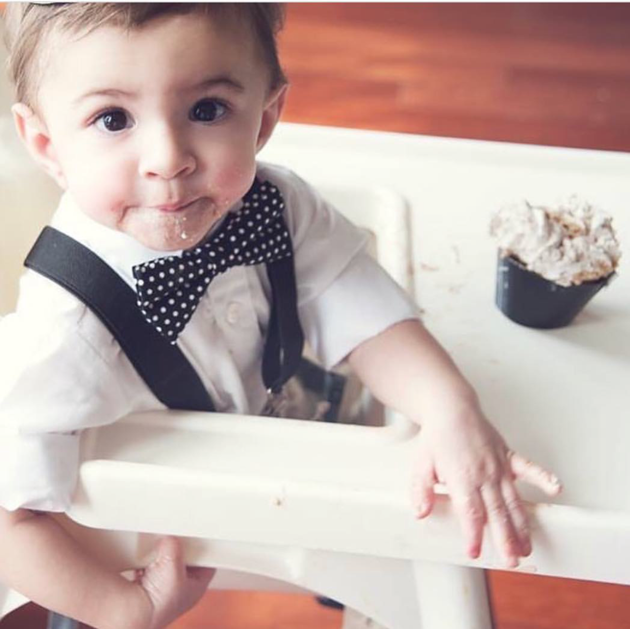 a little boy that is sitting in a chair wearing black suspenders