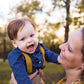 Woman holding a baby outdoors with trees in the background Mustard yellow suspenders