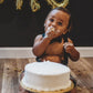 Baby celebrating a first birthday with a cake and gold balloons. black bow tie and suspenders