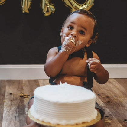 Baby celebrating a first birthday with a cake and gold balloons. black bow tie and suspenders