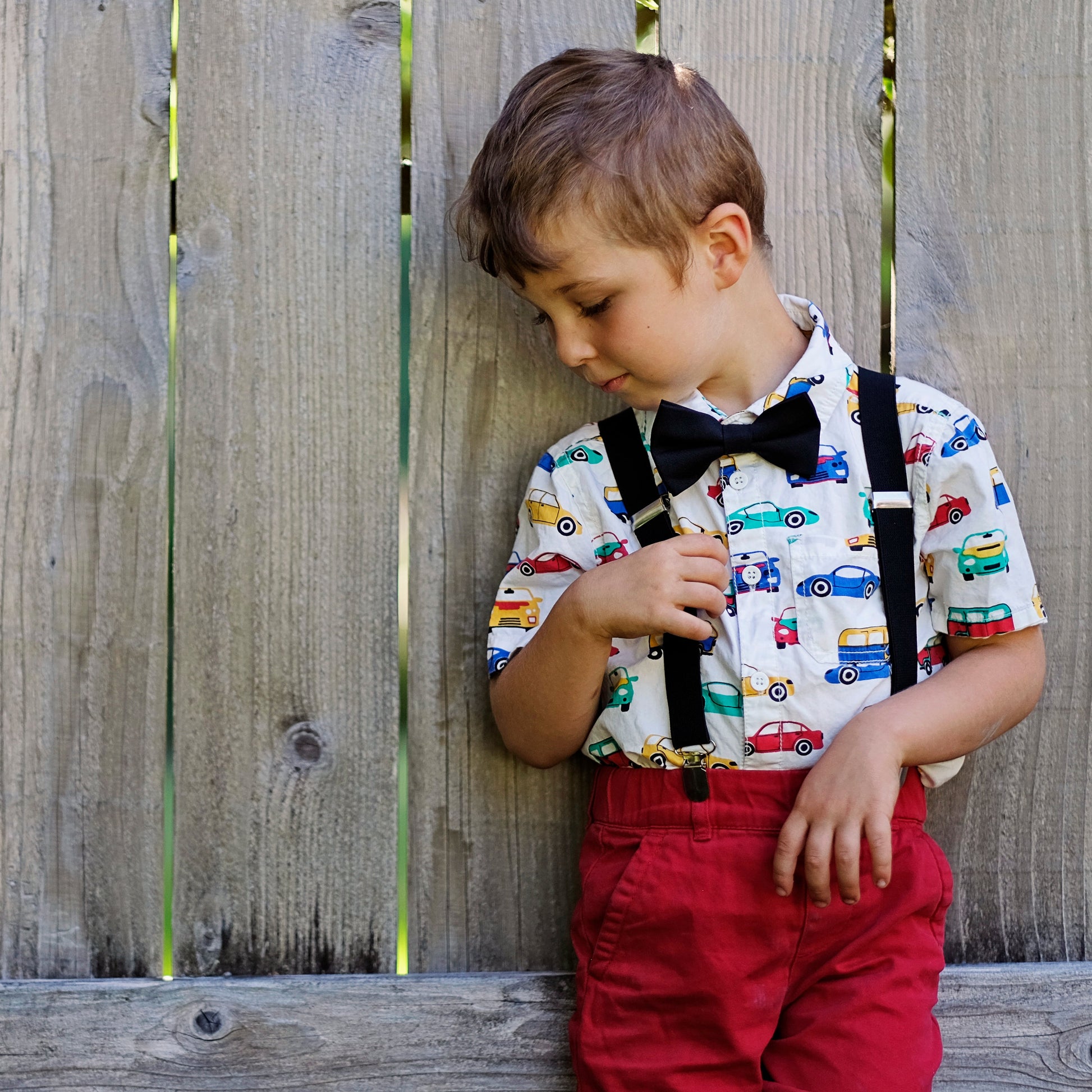 Child wearing suspenders and a colorful shirt against a wooden fence