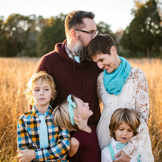 Family of five standing in a field with trees in the background Seafoam bow tie and suspenders
