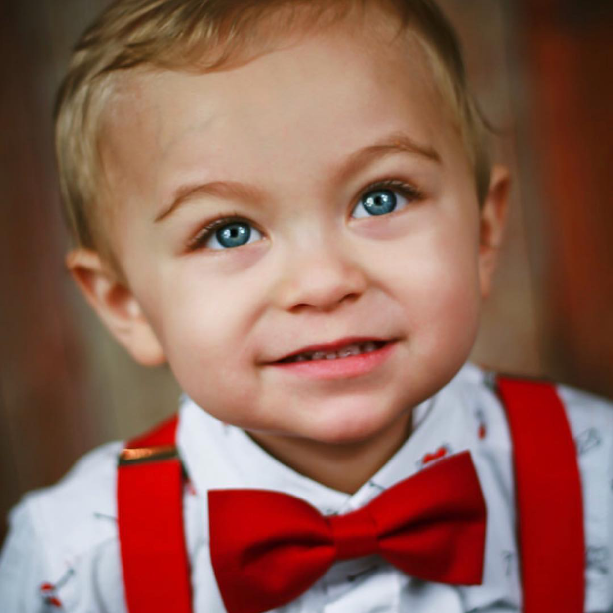 Child wearing a red bow tie and suspenders with a blurred background