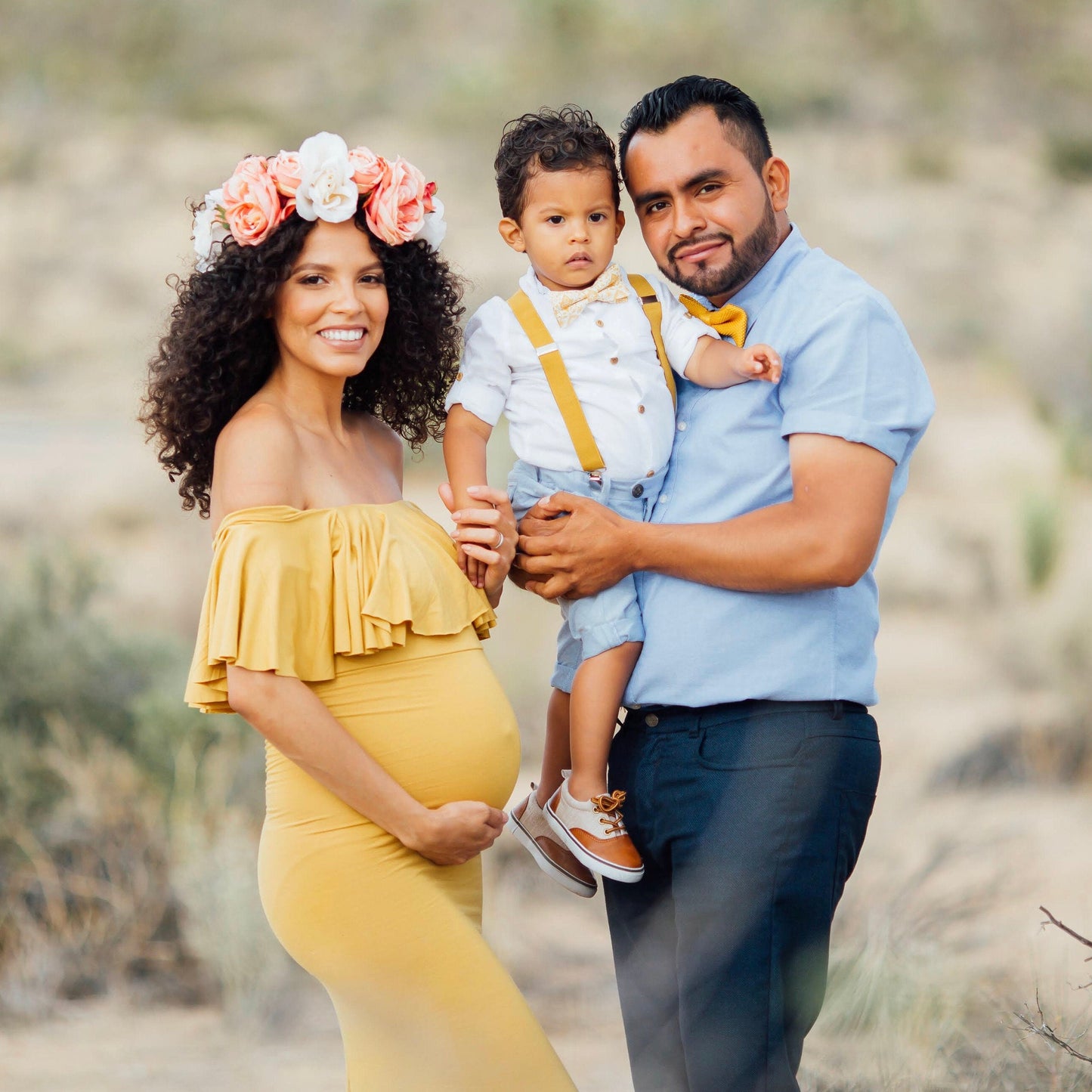 Family of three posing outdoors in a desert-like setting Mustard  yellow bow tie suspenders, pregnancy photo shoot