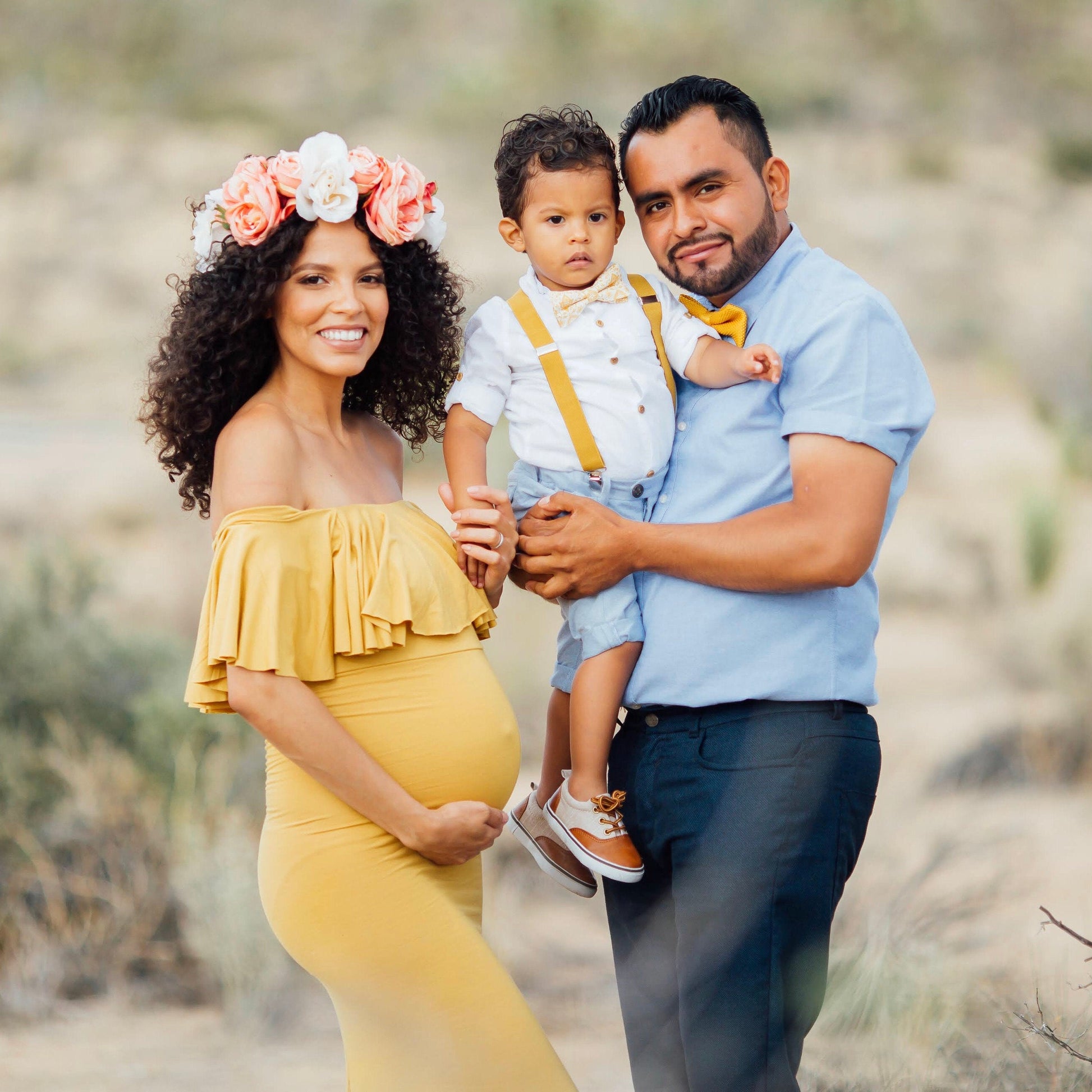 Family of three posing outdoors in a desert-like setting Mustard  yellow bow tie suspenders, pregnancy photo shoot