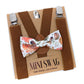 Brown suspenders with a floral bow tie on a 'Mini Swag' branded card.