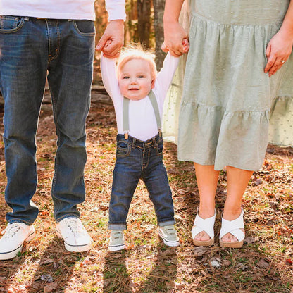 a little boy holding the hand of his parents wearing dusty sage suspenders