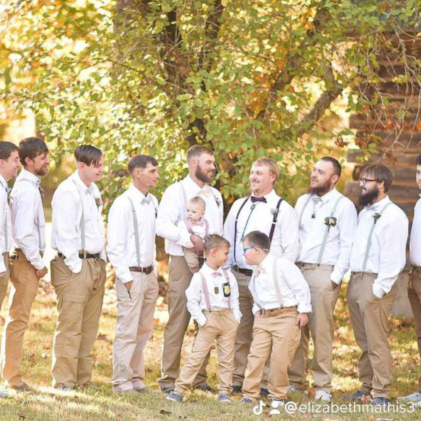 groomsmen wearing dusty sage bow ties and suspenders in white shirts and tan pants standing outdoors with trees in the background