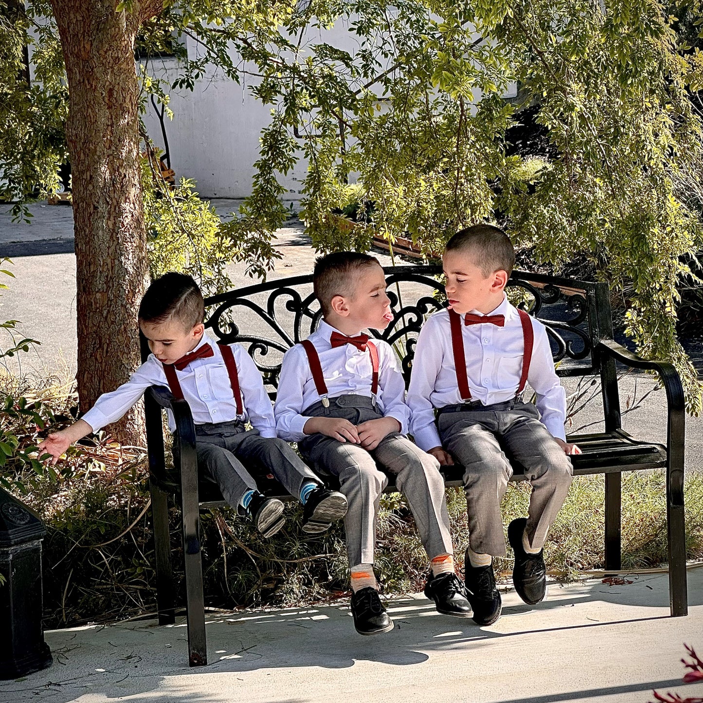 Three young boys ring bearers sitting on a bench wearing matching outfits with suspenders and Cinnamon bow ties.