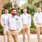 Four groomsmen wearing dusty blue bow ties and suspenders formal attire standing outdoors