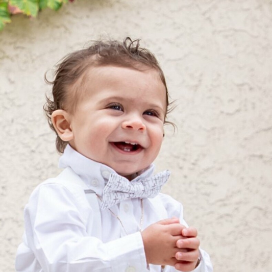 Child wearing a white shirt and christian cross bow tie against a light background 
