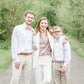 Family of three posing outdoors on a path with greenery. Boy wearing dusty blue bow tie and suspenders