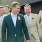 Two men in suits with floral boutonnieres standing outdoors.