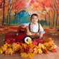 Child sitting in a red toy truck with autumn leaves and a colorful forest background