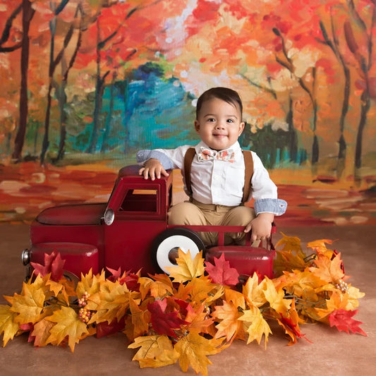 Child sitting in a red toy truck with autumn leaves and a colorful forest background