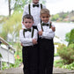 Three young boys in formal attire with suspenders and olive green bow ties standing outdoors.