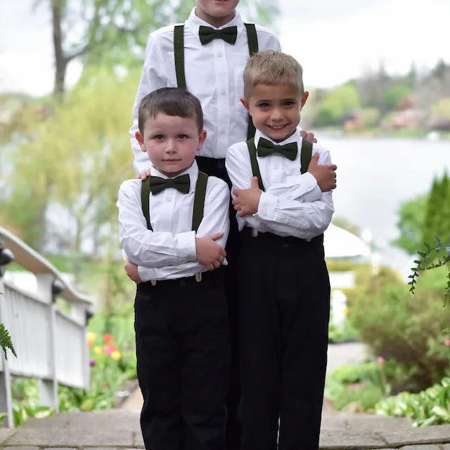 Three young boys in formal attire with suspenders and olive green bow ties standing outdoors.