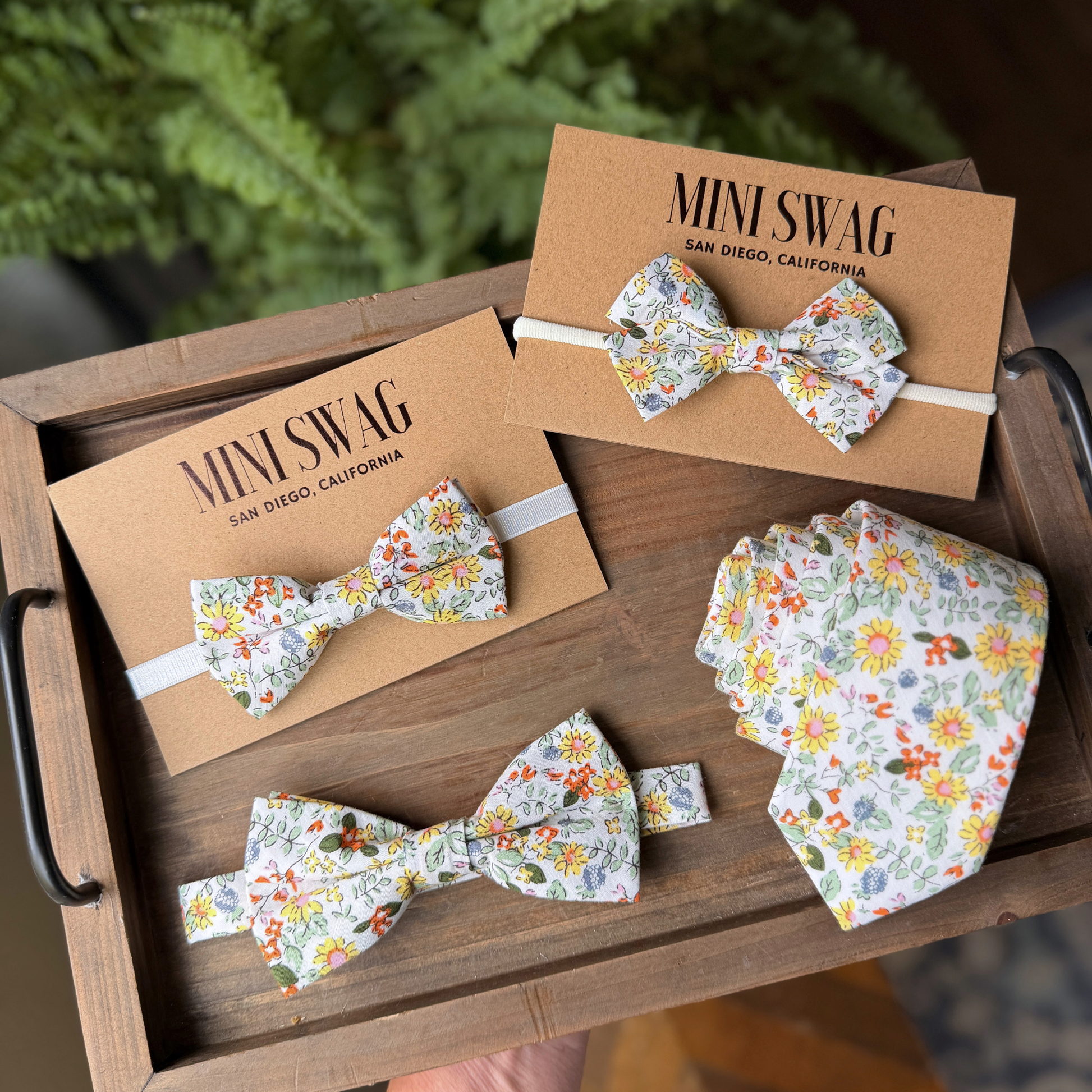 Floral bow ties and headbands on 'Mini Swag' branded cards in a wooden box.