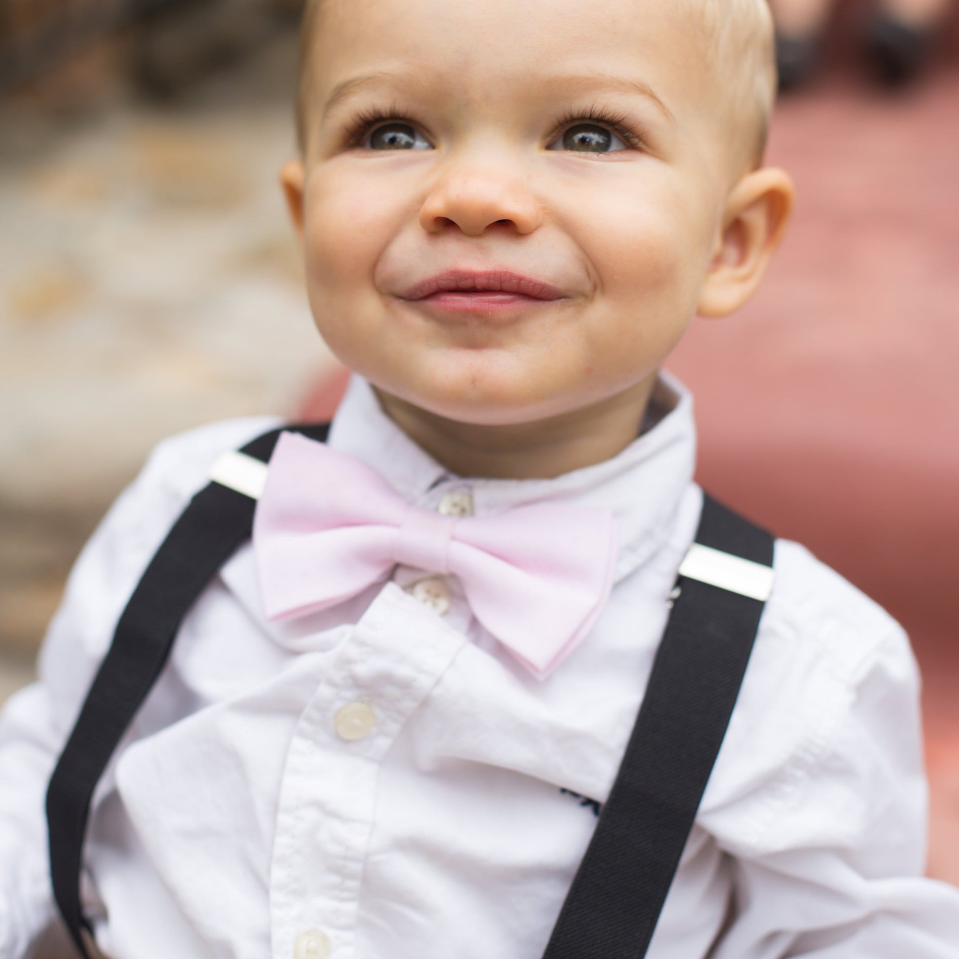 a little boy wearing a pink bow tie and black suspenders